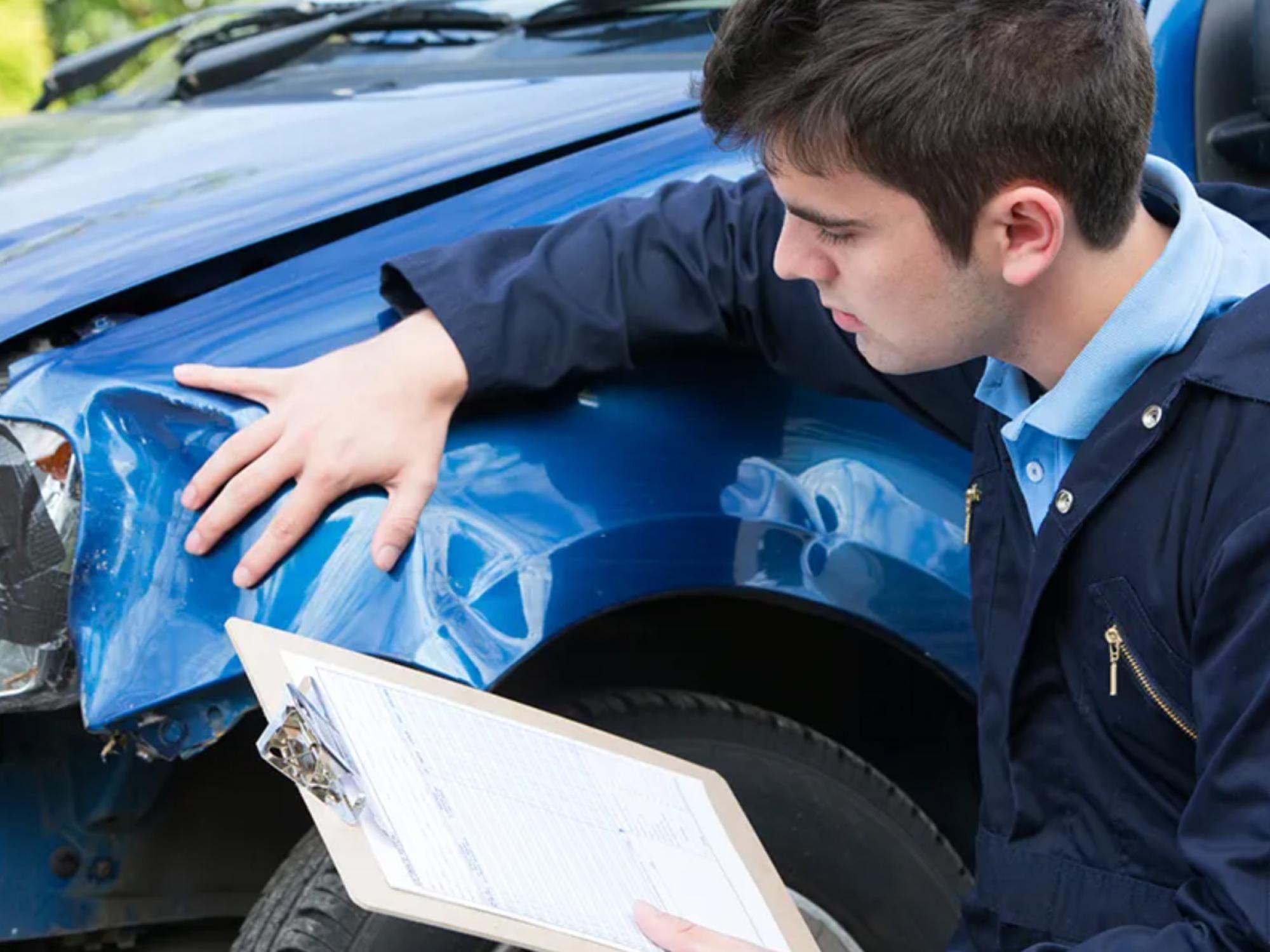 a person with a clipboard, looking at a damaged fender on a blue car